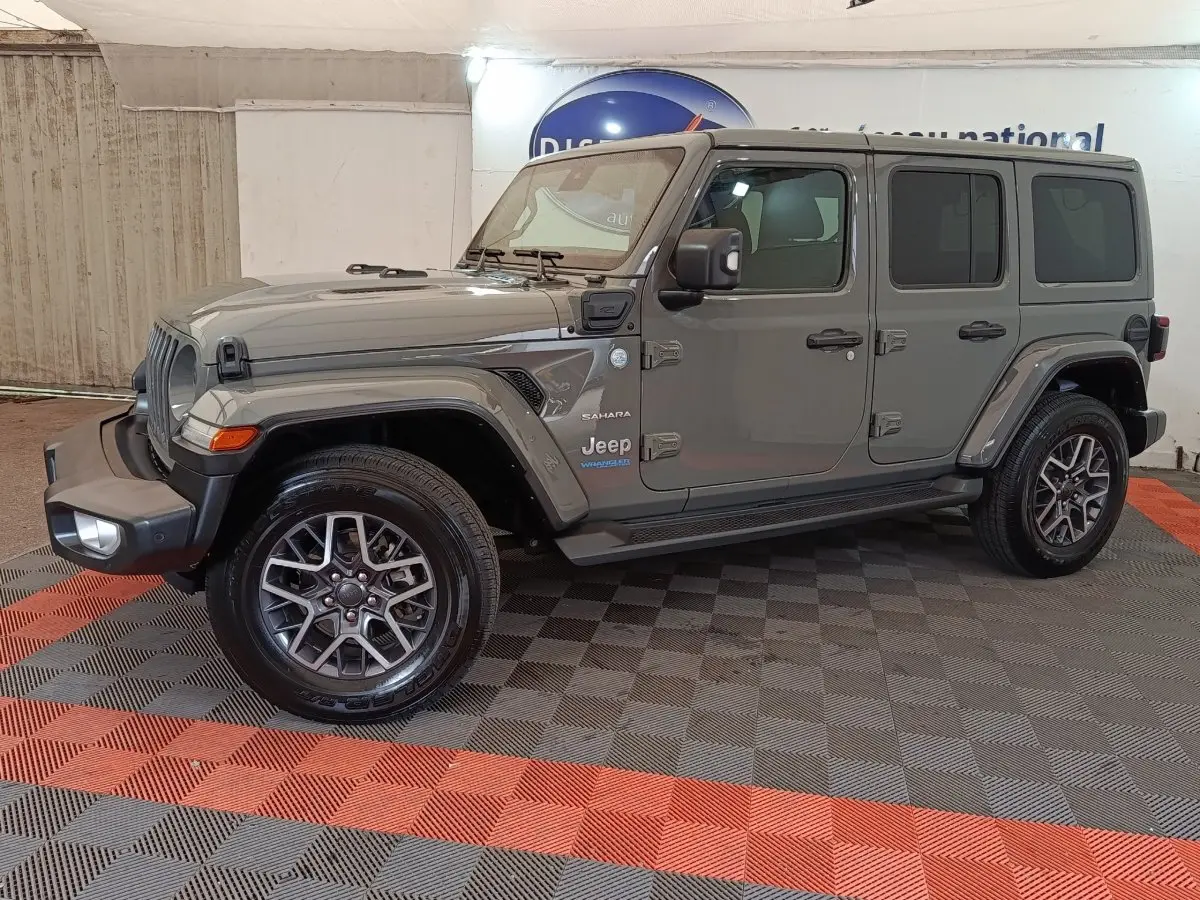 Jeep Wrangler Sahara gris foncé vu de profil côté gauche, avec jantes alliage et toit fermé.