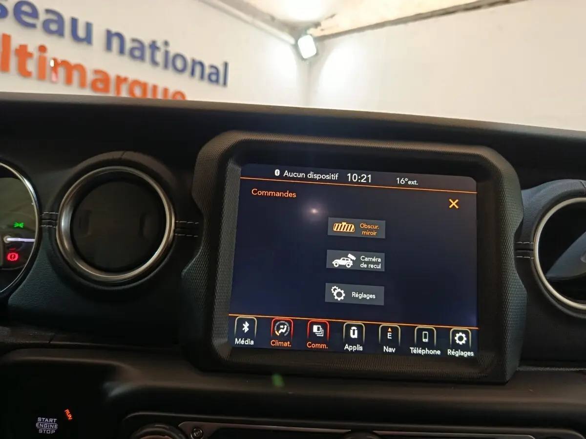Vue rapprochée de l’écran tactile central du tableau de bord du Jeep Wrangler gris foncé, affichant les commandes multimédia et réglages.