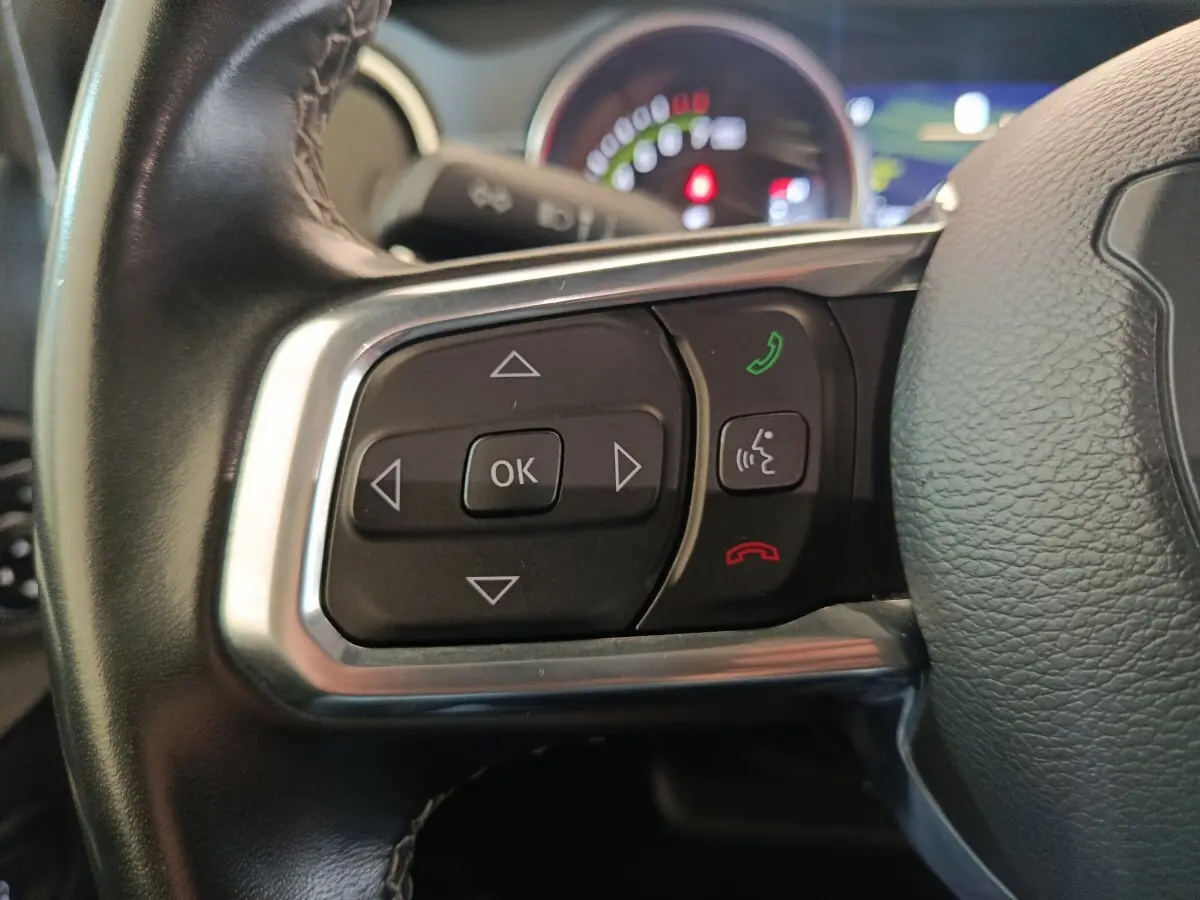 Gros plan sur les commandes gauche du volant cuir du Jeep Wrangler gris foncé, avec tableau de bord flou en arrière-plan.