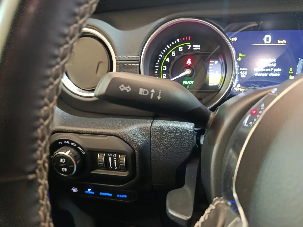 Gros plan sur le tableau de bord et volant cuir du Jeep Wrangler hybride gris foncé, avec affichage numérique et commandes lumineuses.