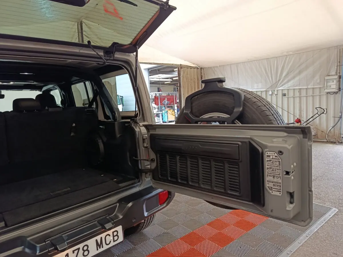 Vue arrière ouverte du Jeep Wrangler gris foncé, montrant le coffre vide et la roue de secours fixée sur la porte.