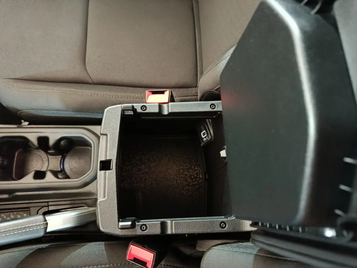 Vue plongeante sur la console centrale ouverte du Jeep Wrangler 2022, montrant un rangement noir entre les sièges gris foncé.