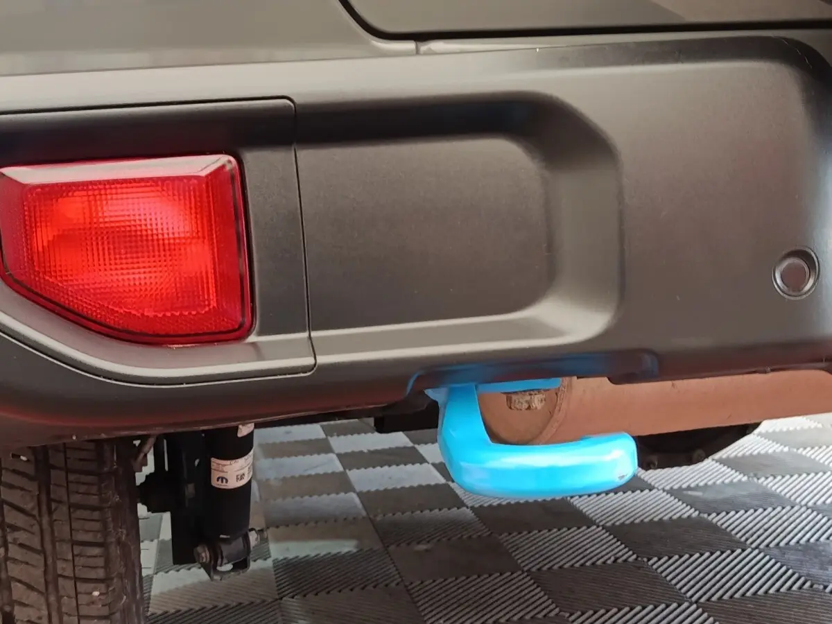 Gros plan sur l'attelage bleu sous le pare-chocs arrière gris foncé du Jeep Wrangler 2022, avec feu arrière rouge visible.