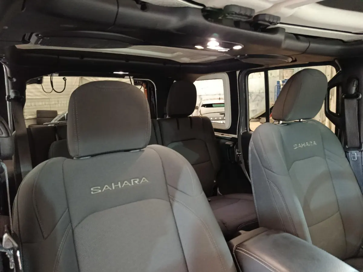 Vue intérieure avant de la Jeep Wrangler Sahara 2022, sièges gris foncé avec logo Sahara brodé, toit cabriolet ouvert.