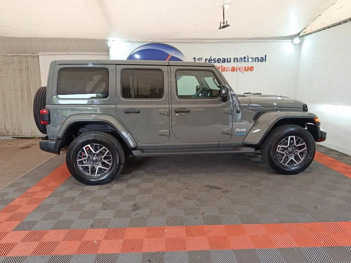 Jeep Wrangler Sahara gris foncé vue de profil côté gauche, avec roue de secours et jantes alliage visibles.