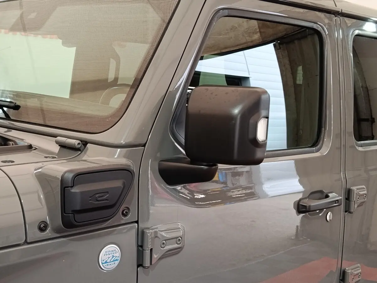 Vue latérale droite d’un Jeep Wrangler gris foncé hybride avec rétroviseur noir et badge Trail Rated 4x4.