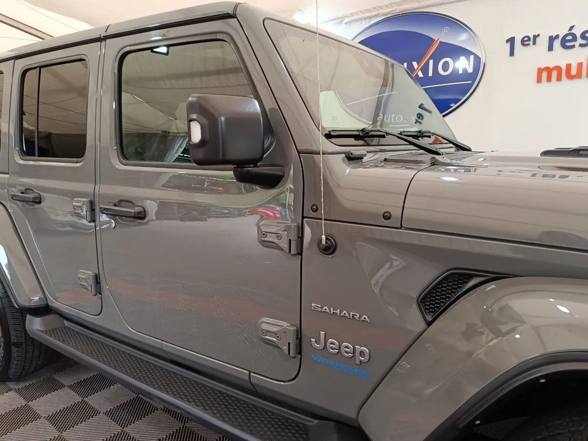 Vue latérale gauche d’un Jeep Wrangler Sahara gris foncé avec logo et détails de la version hybride rechargeable visibles.