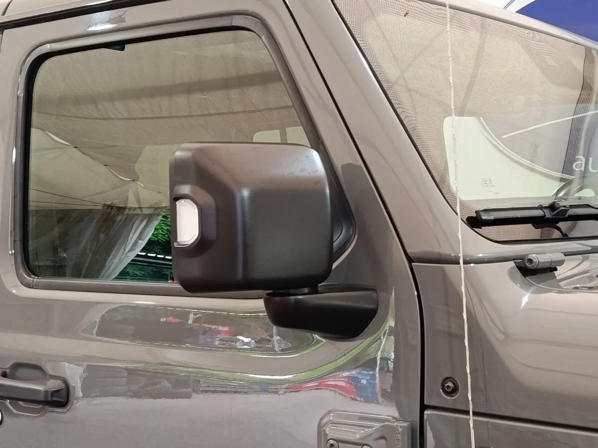 Vue latérale gauche rapprochée d’un Jeep Wrangler gris foncé mettant en valeur la portière et le rétroviseur noir.