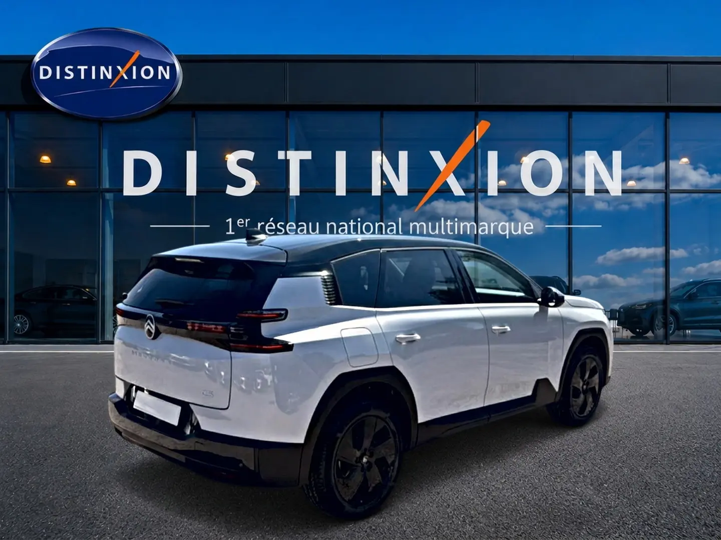 Vue 3/4 arrière droite d'un Citroën C5 Aircross blanc à toit noir avec jantes alliage noires devant un bâtiment Distinxion.