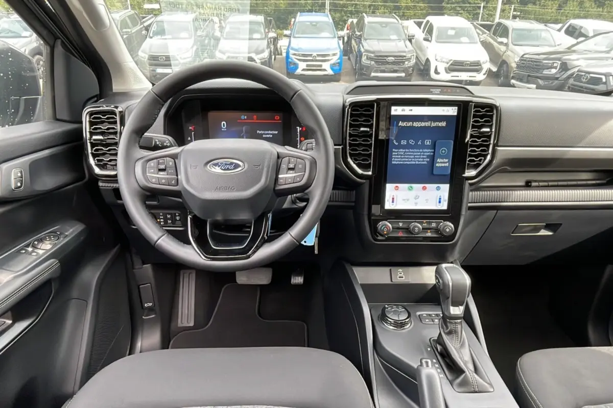 Intérieur du Ford Ranger 2025 gris carbone, vue frontale sur le volant, tableau de bord numérique et écran tactile central.