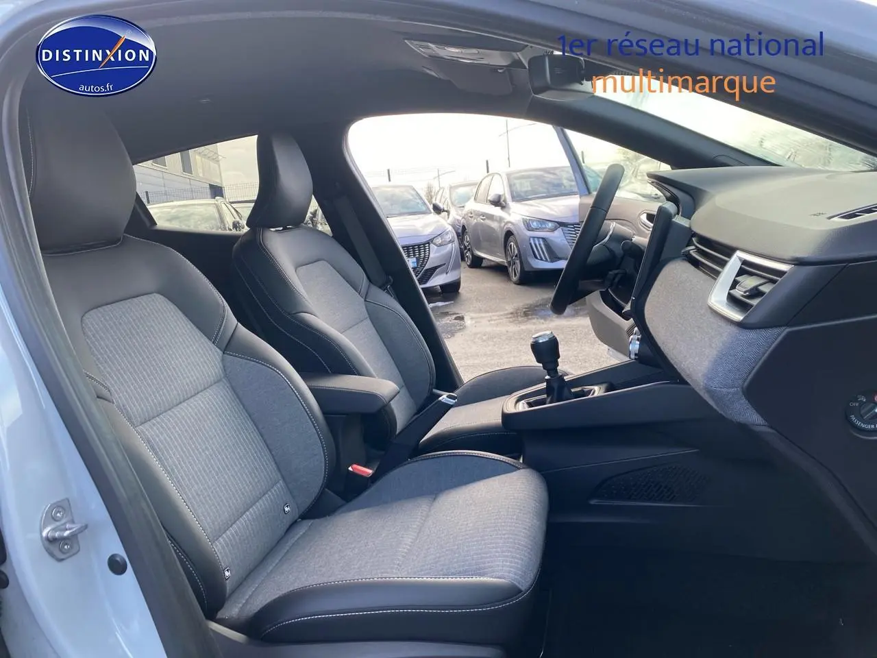 Vue intérieure côté conducteur de la Renault Clio V gris rafale, montrant les sièges tissu et la console centrale avec boîte manuelle.