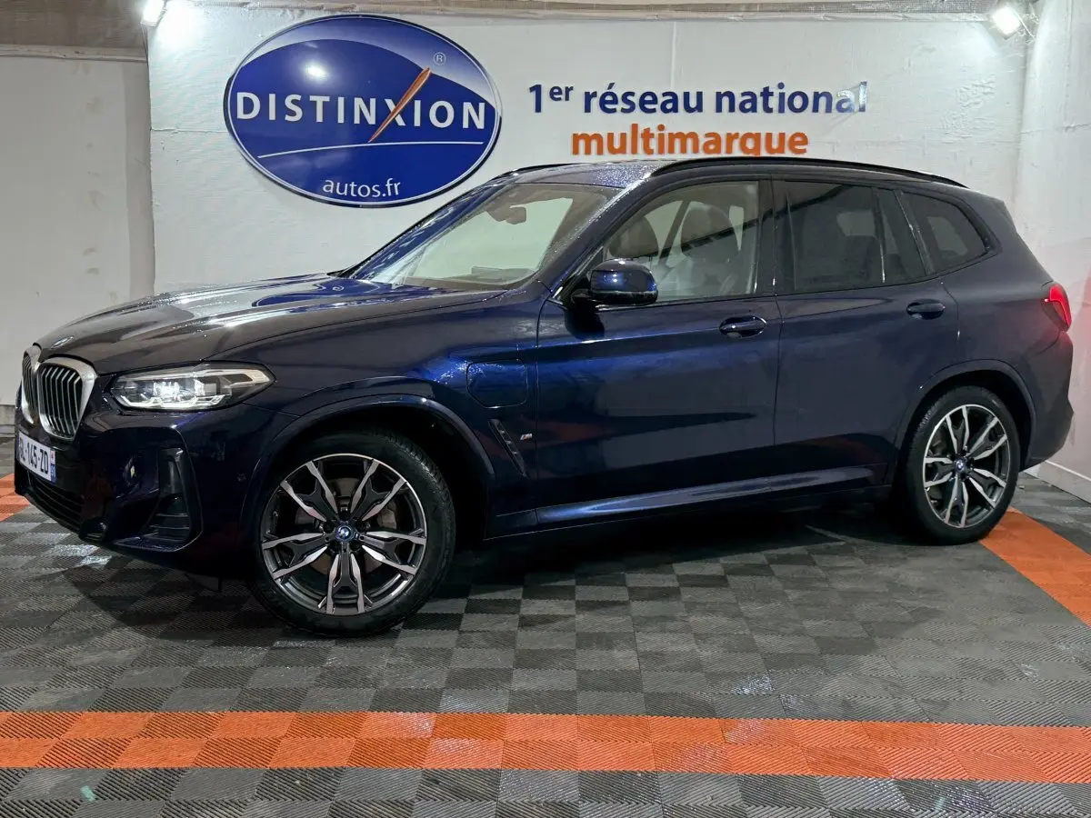 BMW X3 xDrive30e bleu en vue de profil côté gauche dans un showroom avec logo Distinxion en arrière-plan.