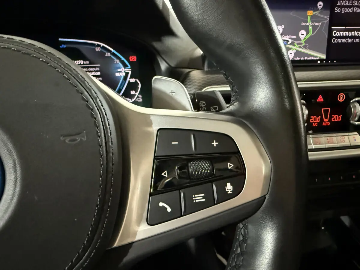Gros plan sur les commandes multifonctions à droite du volant cuir noir du BMW X3 xDrive30e bleu, avec tableau de bord digital.