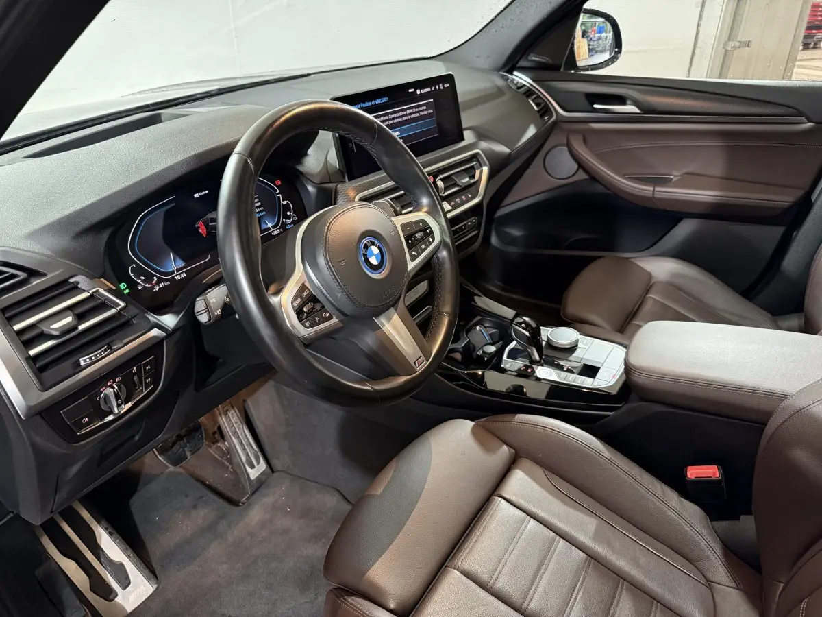 Vue intérieure côté conducteur du BMW X3 xDrive30e 2023 avec tableau de bord digital et sellerie cuir marron.