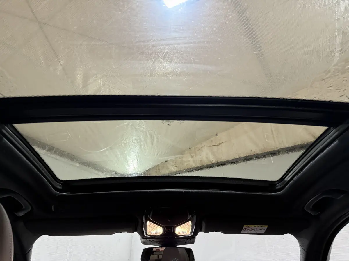 Toit panoramique en verre vu de l'intérieur d'un BMW X3 xDrive30e bleu, avec plafonnier allumé.