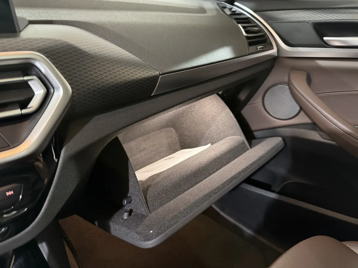 Intérieur BMW X3 xDrive30e 2023, vue côté passager sur boîte à gants ouverte et garnitures marron et noires.