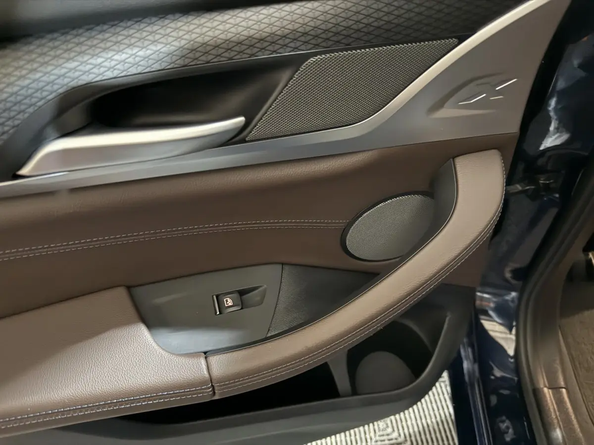 Détail de la porte avant gauche du BMW X3 xDrive30e 2023 en bleu, avec garniture cuir marron et haut-parleur intégré.