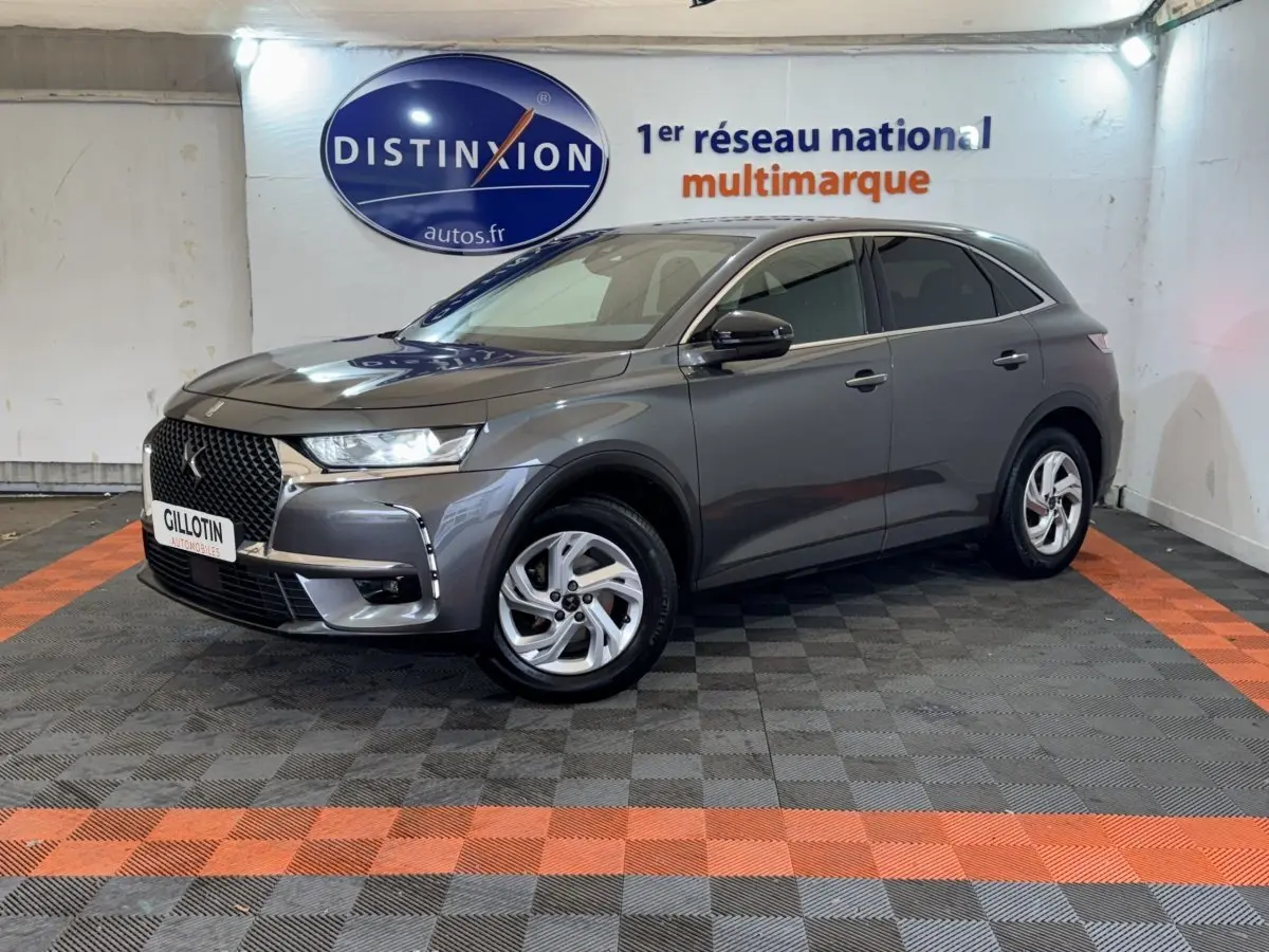 DS7 Crossback gris foncé en 3/4 avant droit, avec calandre distinctive et jantes alliage visibles en intérieur showroom.