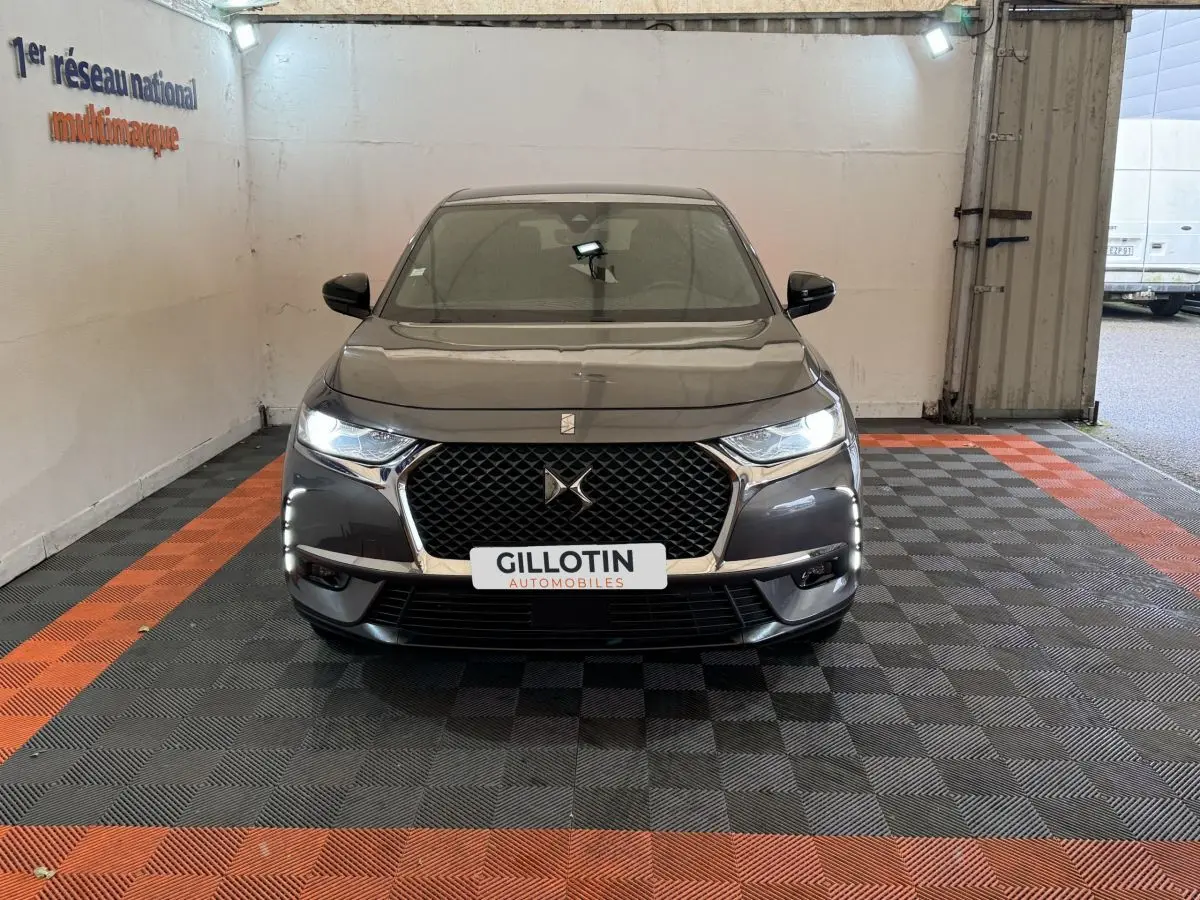 Vue frontale d'un DS7 Crossback gris foncé avec calandre distinctive et phares LED allumés dans un garage.