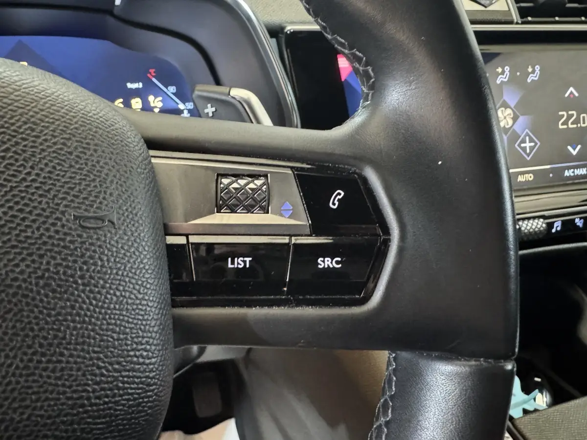 Gros plan sur le volant cuir noir du DS7 Crossback 2020 avec commandes audio et écran tactile de climatisation en arrière-plan.