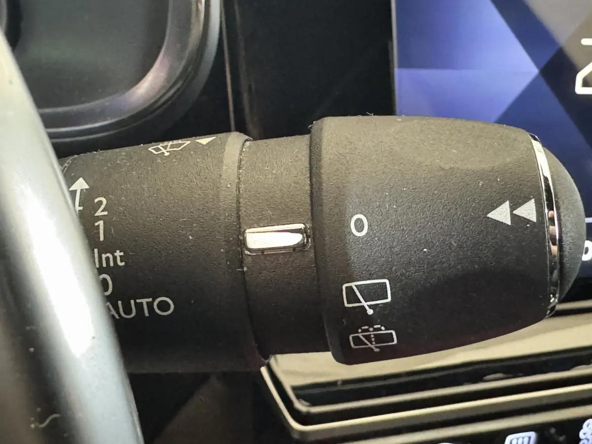 Gros plan sur la commande des essuie-glaces du DS7 Crossback gris foncé, avec tableau de bord numérique en arrière-plan.