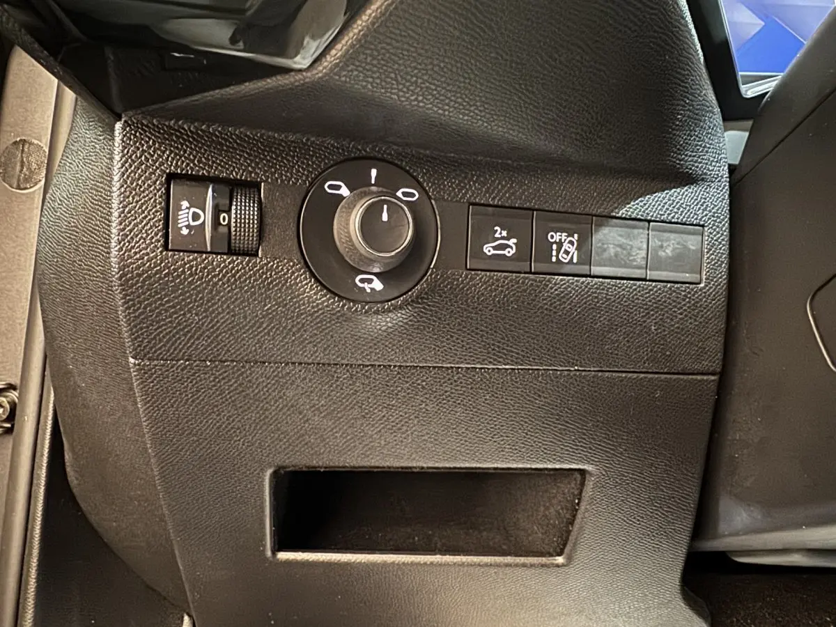 Gros plan sur les commandes noires côté gauche du tableau de bord du DS7 Crossback gris foncé, avec réglage phares et ouverture coffre.