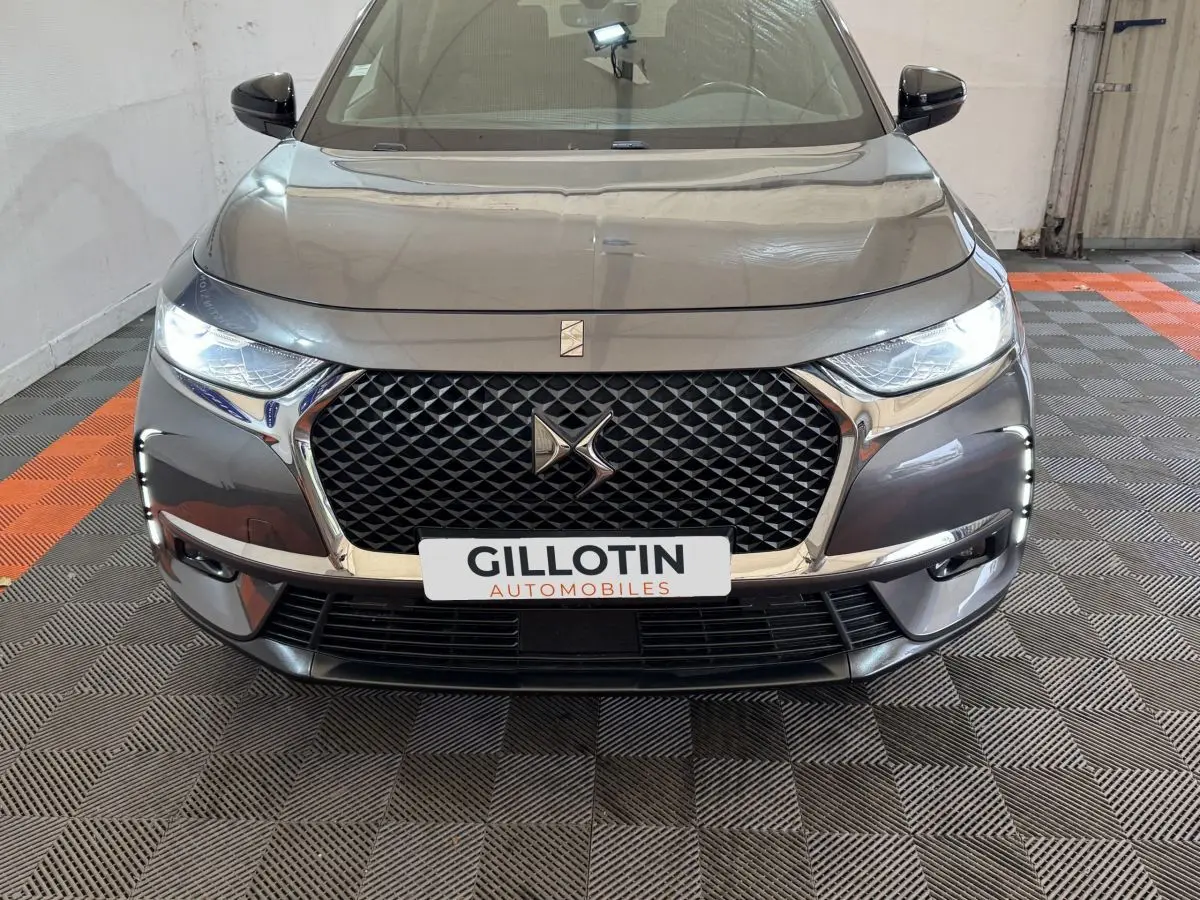 Vue avant d’un DS7 Crossback gris foncé avec calandre hexagonale et feux LED allumés dans un garage.