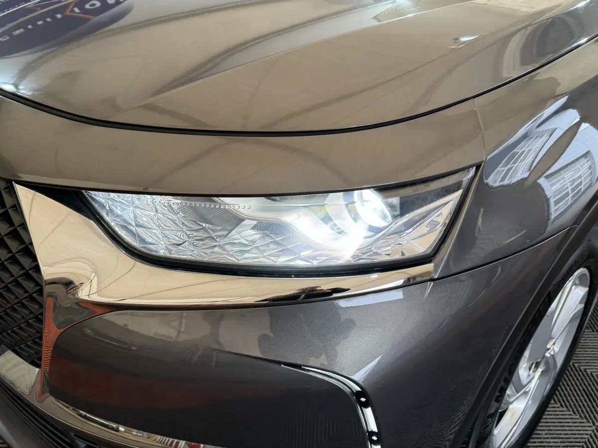 Gros plan sur le phare avant droit allumé d’un DS7 Crossback gris foncé, avec détails chromés autour de la calandre.