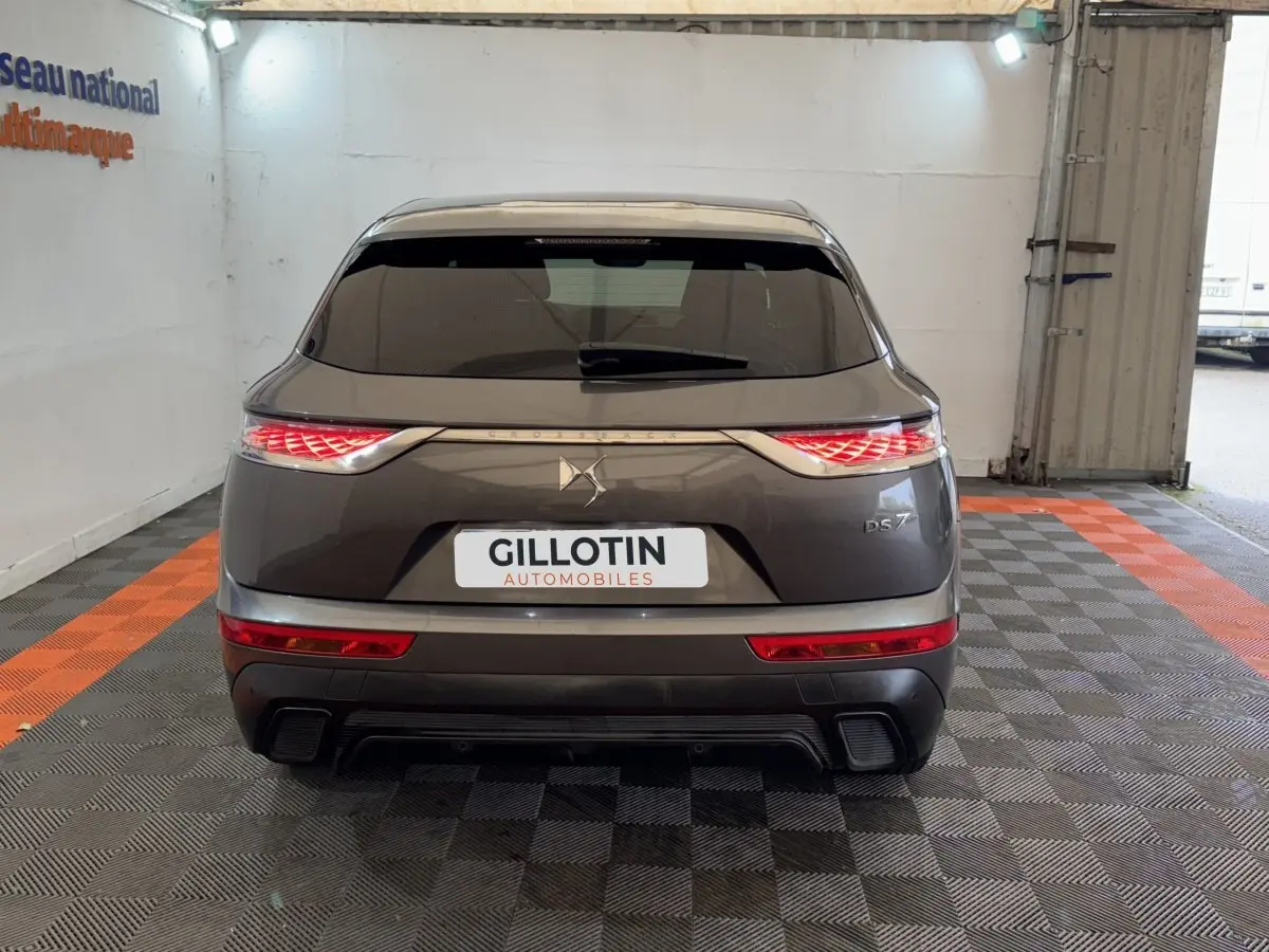 Vue arrière du DS7 Crossback gris foncé avec feux LED distinctifs et logo DS centré sur un fond clair intérieur.