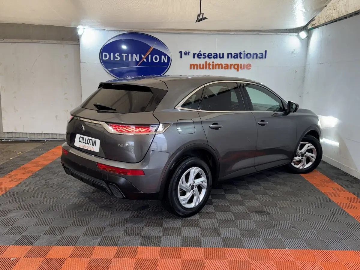 Vue 3/4 arrière droite d’un DS7 Crossback gris foncé stationné en intérieur avec feux arrière allumés.