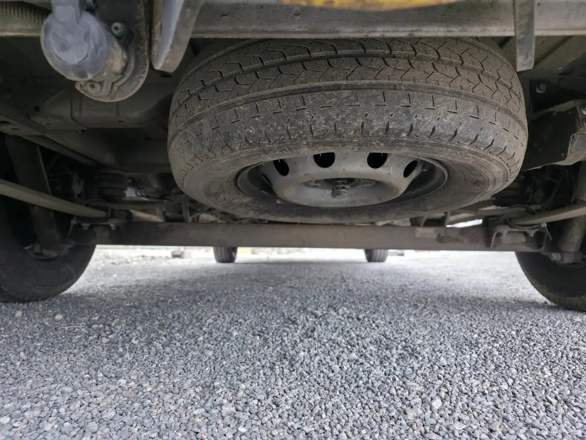 Vue en contre-plongée sous un Peugeot Boxer Fourgon blanc, montrant la roue de secours sous le châssis arrière.