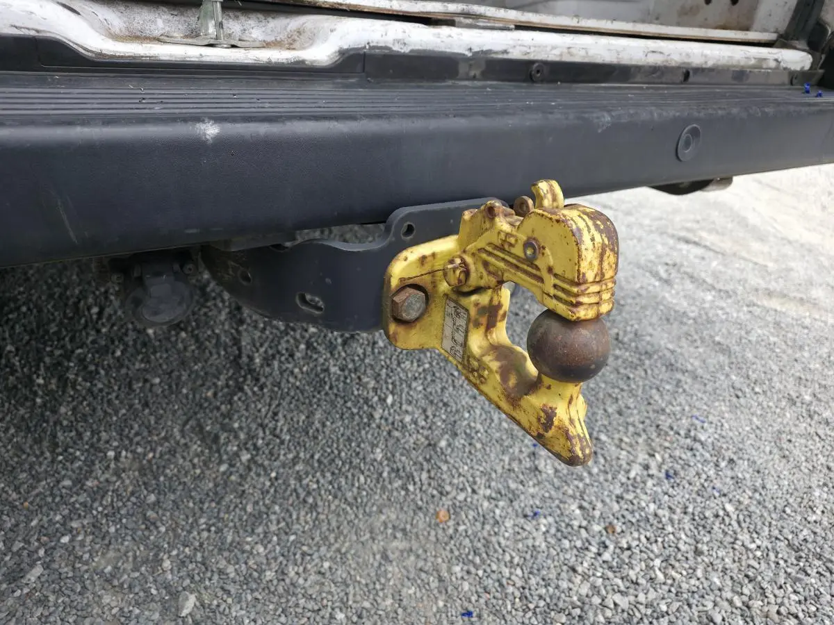Gros plan sur le crochet d'attelage jaune rouillé fixé à l'arrière d'un Peugeot Boxer Fourgon blanc.