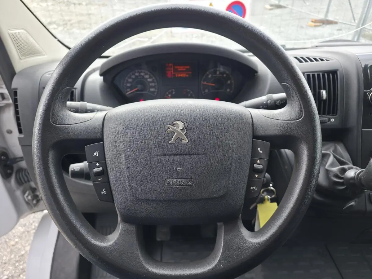 Vue rapprochée du volant noir avec logo Peugeot du Boxer Fourgon 2022, tableau de bord et levier de vitesses visibles.