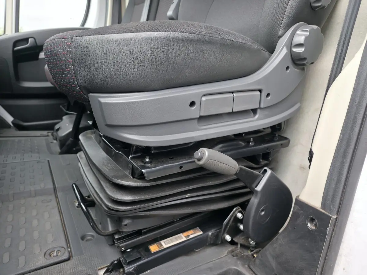 Gros plan sur le siège conducteur suspendu gris foncé du Peugeot Boxer Fourgon blanc, côté gauche intérieur cabine.