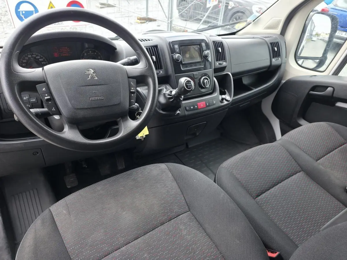 Vue intérieure côté conducteur du Peugeot Boxer Fourgon 2022, volant noir, sièges tissu gris foncé avec motifs rouges.