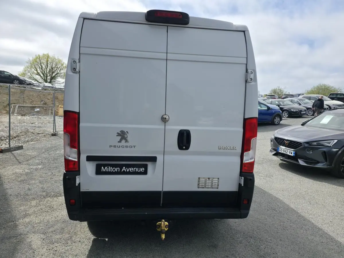 Vue arrière d’un Peugeot Boxer blanc avec crochet d’attelage et portes battantes fermées sur parking.