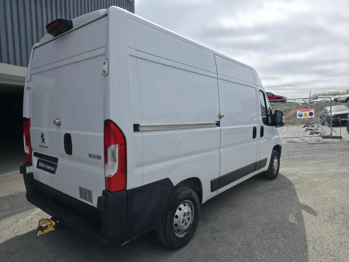 Vue 3/4 arrière droite du Peugeot Boxer Fourgon blanc avec crochet d'attelage et baguettes latérales noires.