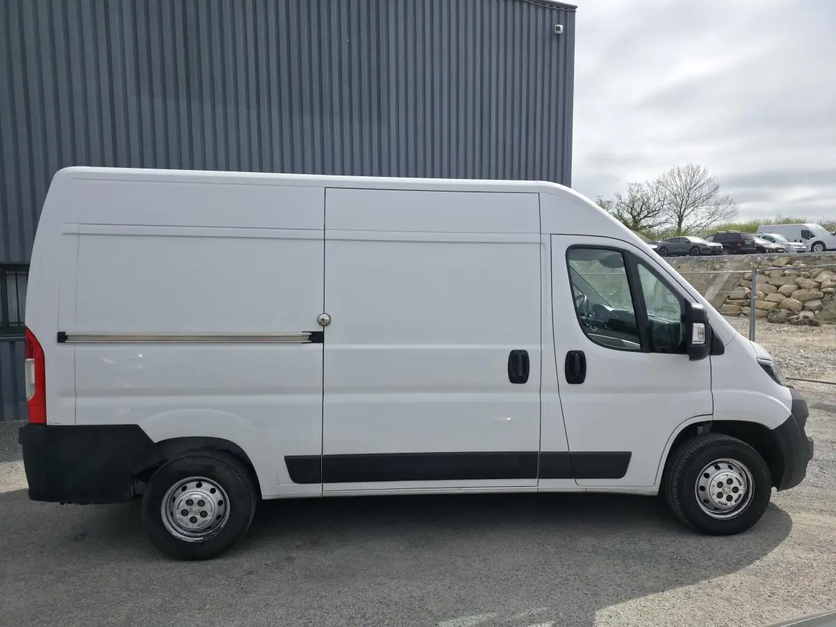 Peugeot Boxer Fourgon blanc vu de profil côté droit, avec porte latérale coulissante et enjoliveurs noirs.