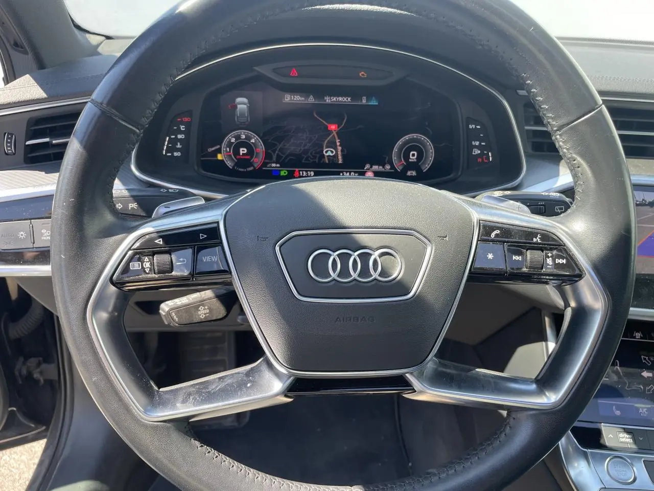 Vue rapprochée du volant en cuir multifonction d’une Audi A6 2019, avec tableau de bord numérique et commandes intégrées.