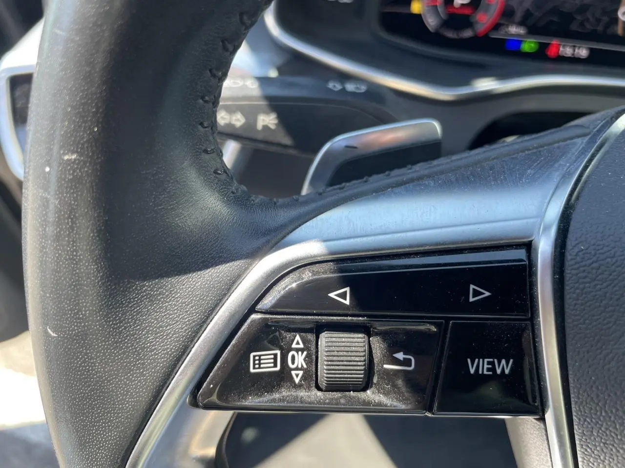 Gros plan sur les commandes gauche du volant en cuir noir de l'Audi A6 V Avant 45 TDI 2019.