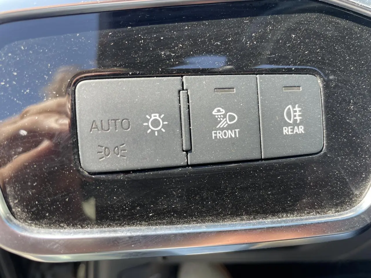 Gros plan sur les boutons de commande d’éclairage automatique et antibrouillard avant/arrière sur tableau de bord noir brillant.