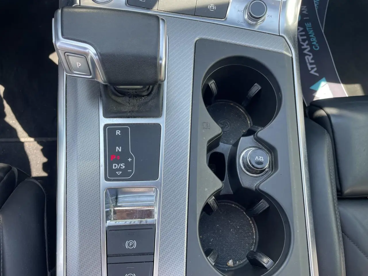 Gros plan sur la console centrale de l’Audi A6 noire, avec levier de vitesse automatique et porte-gobelets.