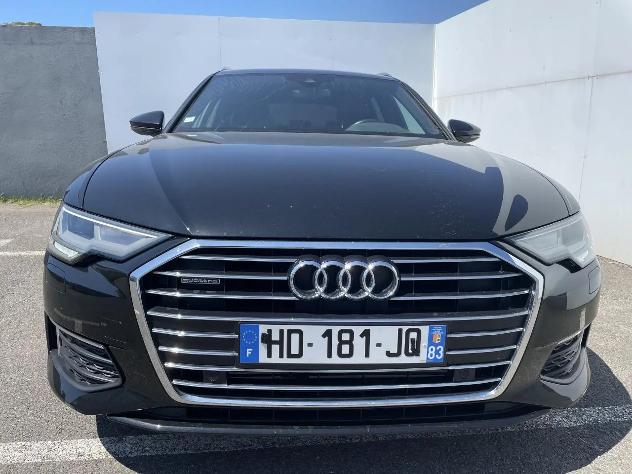 Vue avant d'une Audi A6 noire métal 2019 avec calandre chromée et phares Full LED allumés.