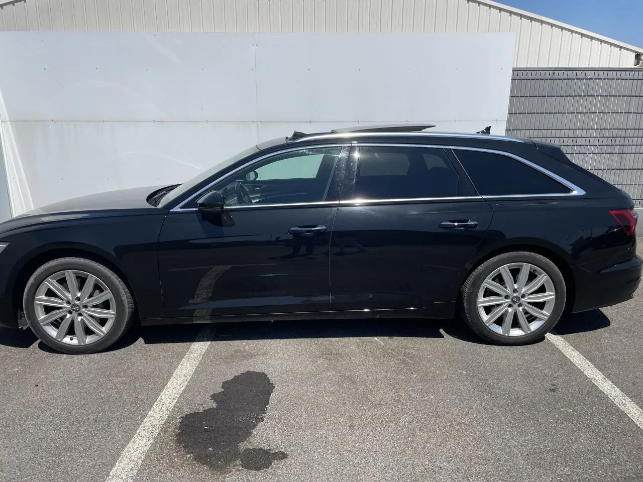 Profil latéral droit d'une Audi A6 Avant noire métallisée avec jantes aluminium 10 branches et vitres surteintées.