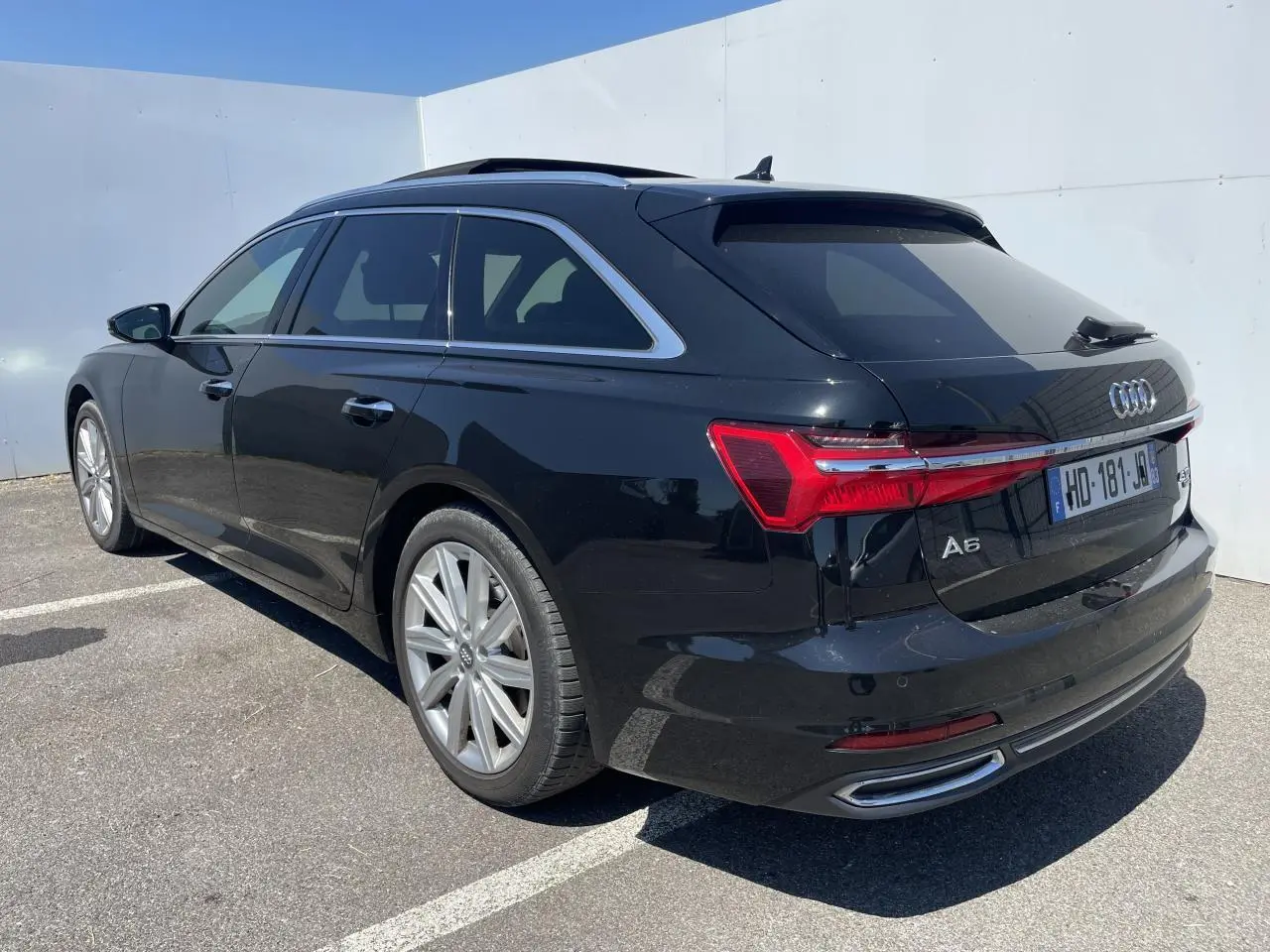 Audi A6 Avant noir métal vue 3/4 arrière droit, jantes 19 pouces et feux arrière LED distinctifs.