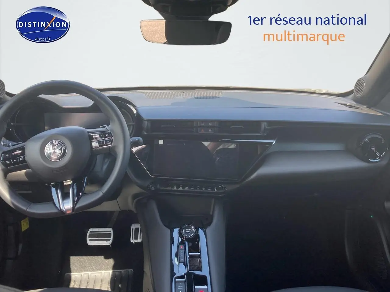 Vue intérieure frontale de l'Alfa Romeo Junior 1.2 hybride 2026, tableau de bord noir avec écran tactile et volant multifonction.
