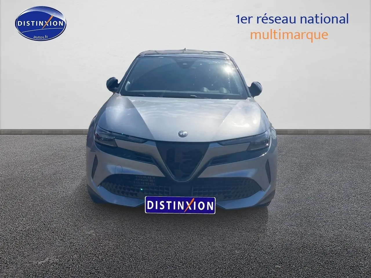Vue frontale d'une Alfa Romeo Junior 1.2 hybride 2026 gris métallisé avec calandre caractéristique en V et phares LED fins.