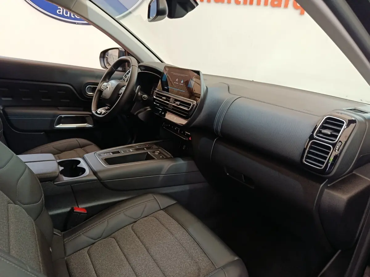 Vue intérieure côté conducteur du tableau de bord et console centrale du Citroën C5 Aircross 2024 noir avec écran tactile et volant cuir.