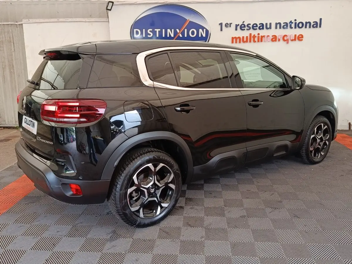 Vue 3/4 arrière droite d'un Citroën C5 Aircross noir 2024 avec jantes distinctives et barres de toit chromées.