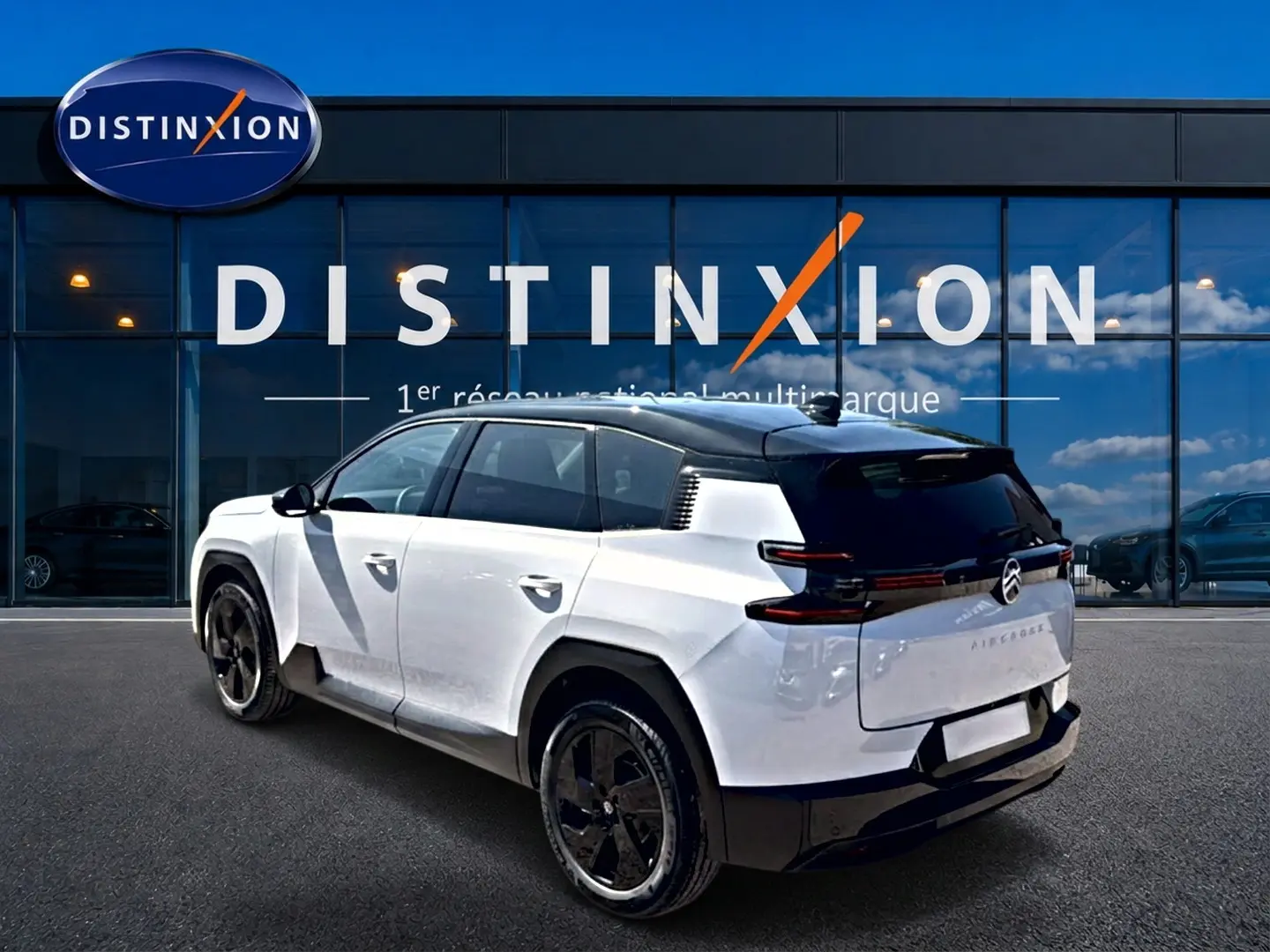 Vue 3/4 arrière droite du Citroën C5 Aircross hybride blanc avec toit noir et jantes alliage noires devant un showroom Distinxion.